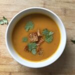 a bowl of kabocha squash soup topped with coriander and croutons.