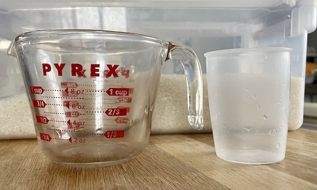 a pyrex metric measuring cup next to a rice cooker cup.