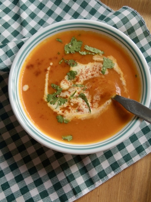 A bowl of carrot and sweet pepper soup with a metal spoon on a green plaid napkin.