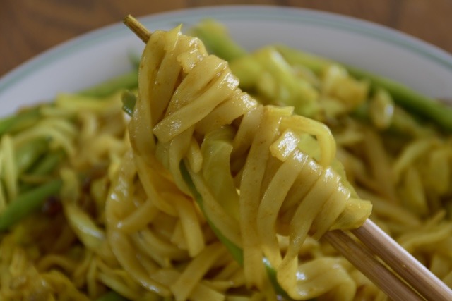 a close up shot of turmeric yaki udon on chopsticks.