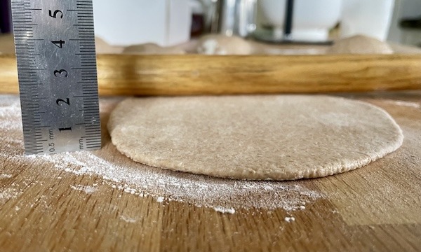 a rolled out pita bread next to a ruler to measure thickness.