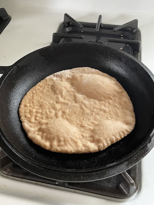 pita bread in a cast iron just beginning to puff up