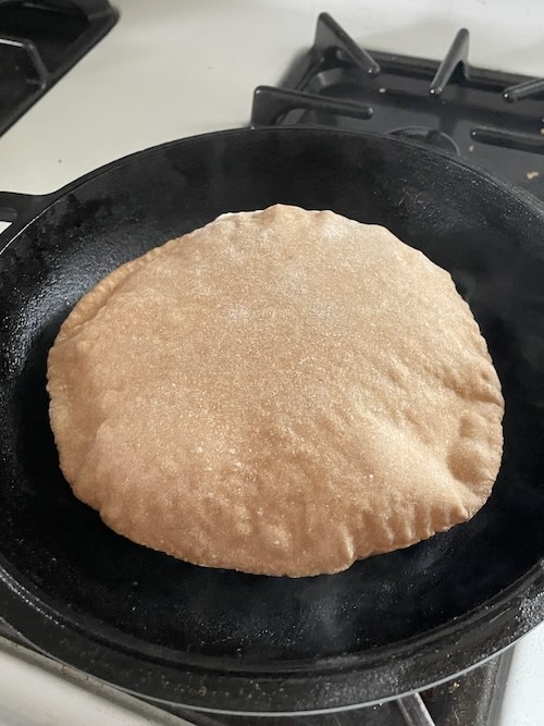 pita bread in a cast iron that is completely puffed up.