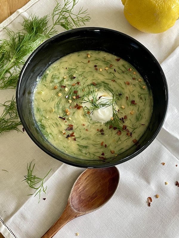 dill lentil soup in a bowl next to a wooden spoon, a lemon, and some dill.