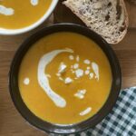 Bowls of kabocha ginger soup next to sliced bread.