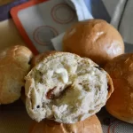 A raisin bun torn open to reveal the texture inside with some butter on top.