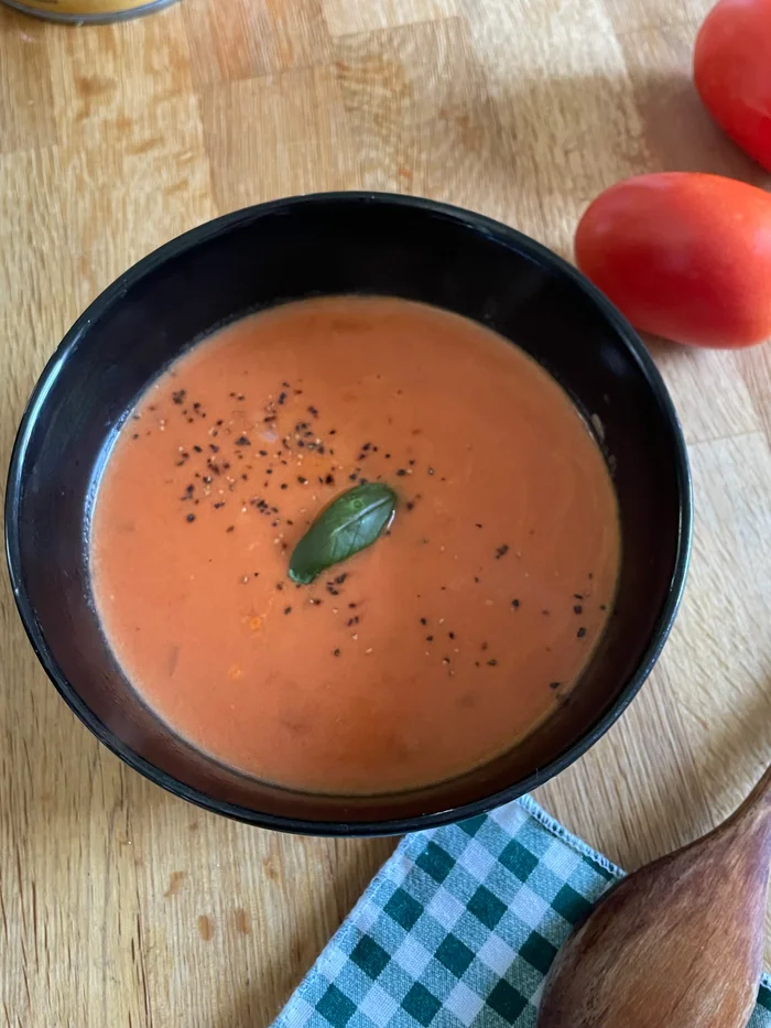 a bowl of tomato coconut cream soup with tomatoes in the background.