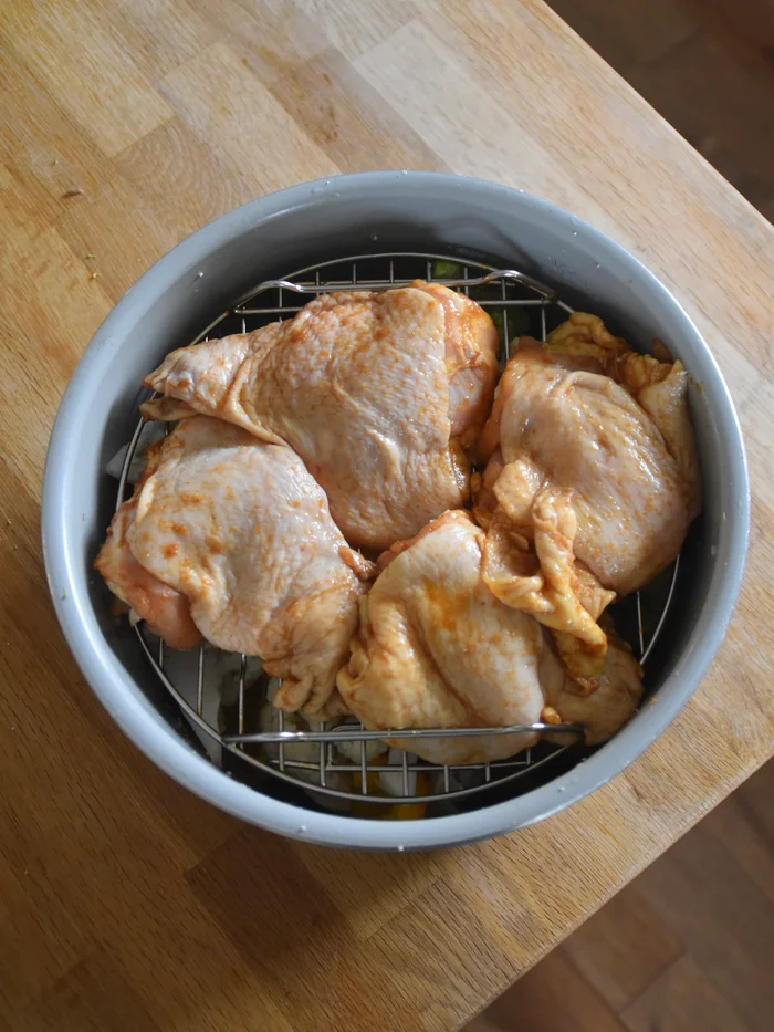 Marinated chicken thighs on a metal rack on top of vegetables, ready for air frying.