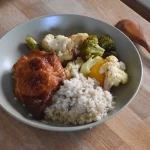 Soy sauce air fryer chicken thighs and vegetables with brown rice on a plate.